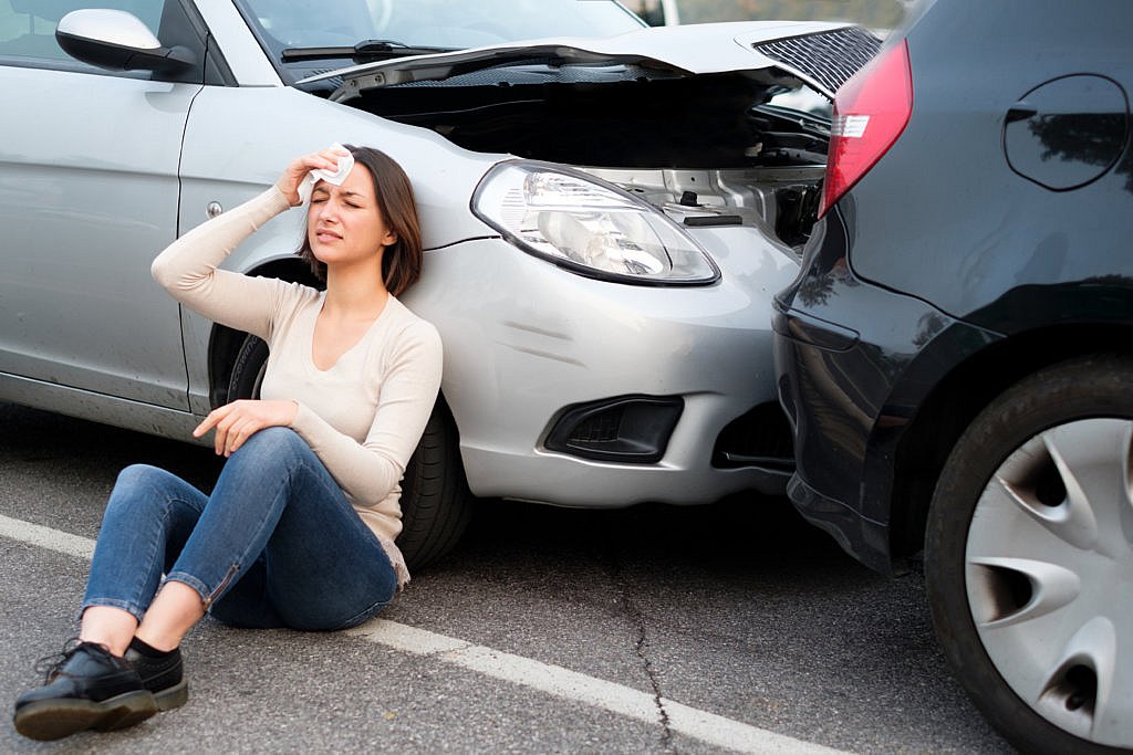 Woman sitting next to damaged car